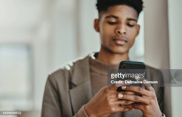 黒人男性、電話、ソーシャルメディアでの入力、スクロール、真面目な顔でオンラインを閲覧する。若い男性、スマートフォンを持ち、研究、チャットやコミュニケーションの楽しみ、メッ� - black boy ストックフォトと画像