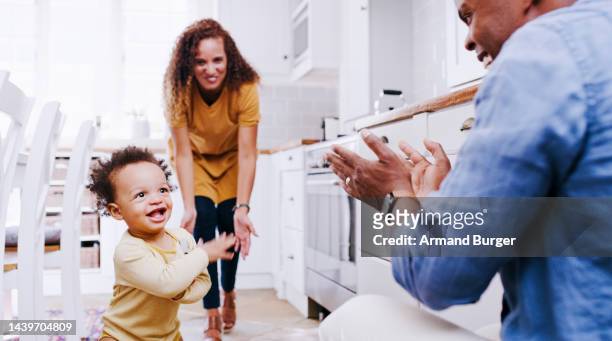 clapping hands, parents and child walking in the kitchen for the first time at the family home. happy, celebrate and family cheering with happiness and pride for baby boy taking steps in their house. - parents cheering stock pictures, royalty-free photos & images