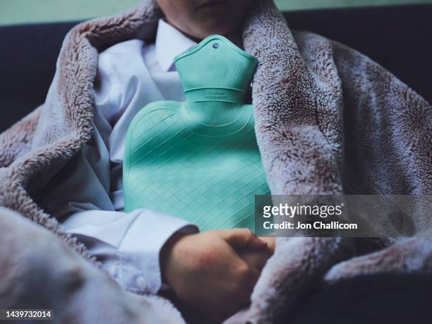 a young child is wrapped in a blanket holding a hot water bottle. - cold temperature stock-fotos und bilder