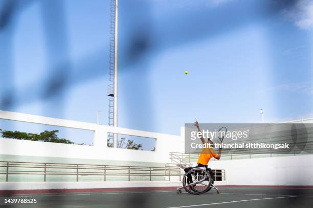 disabled man playing and practicing wheelchair tennis at outdoor tennis court. - wheelchair tennis stock pictures, royalty-free photos & images