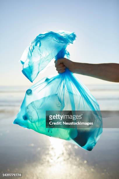 hand of man holding garbage in plastic bag - plastic pollution beach stock pictures, royalty-free photos & images
