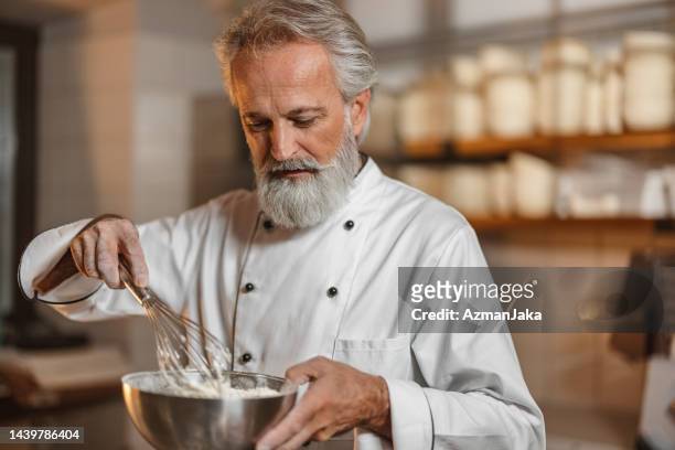 boulanger caucasien mélangeant une pâte avec un fouet à main dans la cuisine - baker smelling bread photos et images de collection