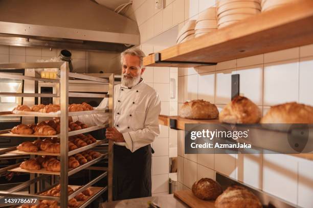 male baker pushing a baking tray trolley full of croissants - baker smelling bread stockfoto's en -beelden