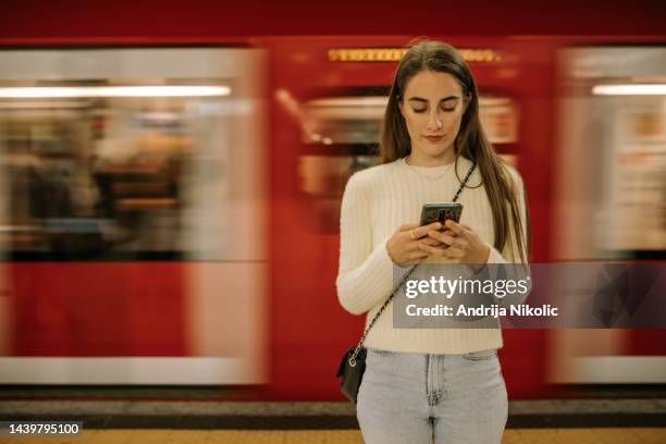 jeune femme à la station de métro utilisant son mobile en attendant - femme métro photos et images de collection