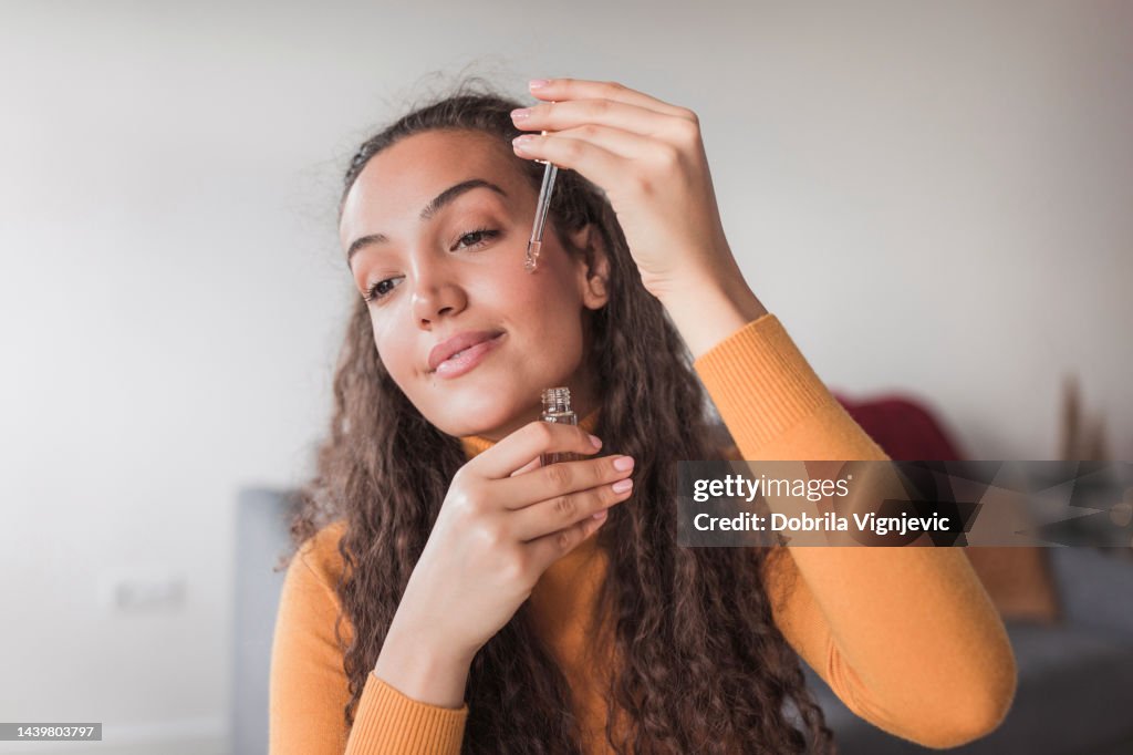 Young satisfied woman using face oil in her daily skin routine