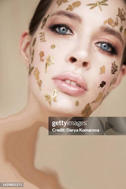 a young woman in a beige suit stands on a beige background with gold decorative stickers on the face with copy space. the beauty concept, halloween, party, makeup, meadow, summer or insects lover, surreal life, the transience of time. - girl power stickers stock pictures, royalty-free photos & images