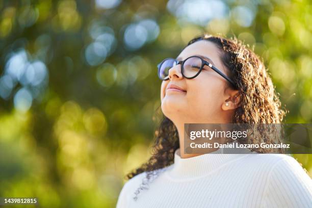 stock photo of curly woman in wearing eyeglasses breathing fresh air in autumn in forest - fresh air breathing stockfoto's en -beelden