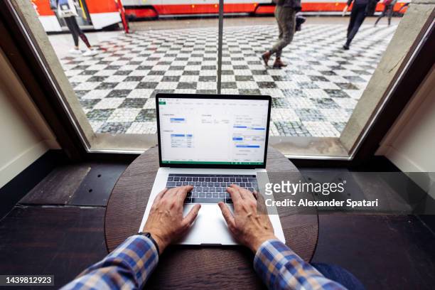 man working on a laptop in a cafe by the window, personal perspective view - filmperspektive stock-fotos und bilder