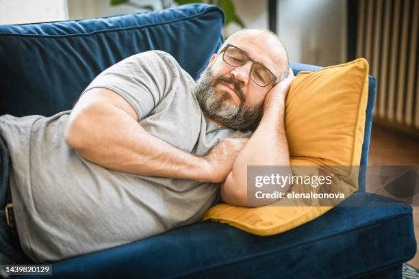 man resting in a room on a blue sofa - couch potato stock pictures, royalty-free photos & images