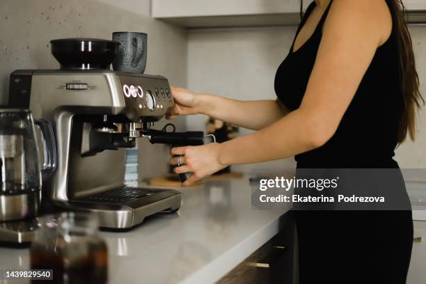 girl at home in the kitchen in black clothes makes coffee in a coffee machine - kaffeemaschine stock-fotos und bilder