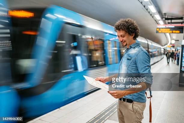 young male tourist reading a map while waiting for a subway train in stockholm - stockholm map stock pictures, royalty-free photos & images