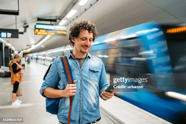 young man using phone while waiting for a subway train in stockholm - subway stock pictures, royalty-free photos & images