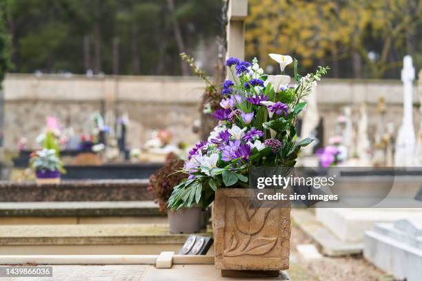 basket of flowers in a cemetery seen from a side angle to the graves in a row with several flowers in the background. - funeral background stock pictures, royalty-free photos & images