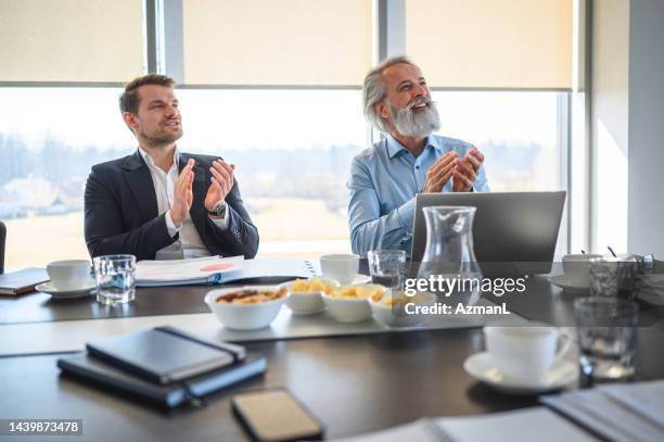 lächelnde mittelerwachsene und reife männer klatschen, während sie an einem konferenztisch sitzen - breakfast meeting stock-fotos und bilder