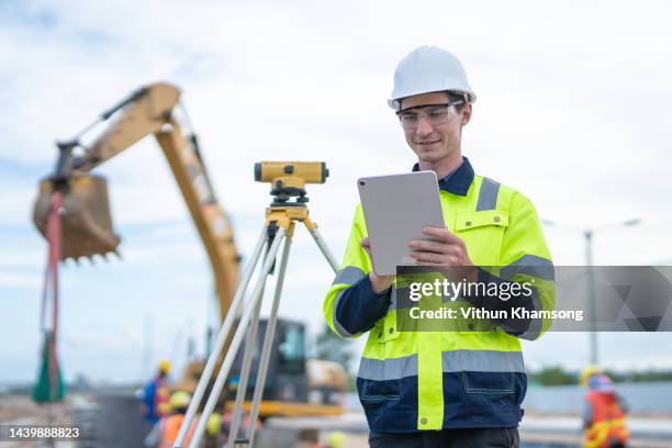 male engineer standing with tablet at construction site survey equipment background - land surveyor stock pictures, royalty-free photos & images