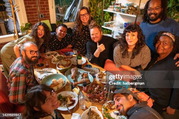 group portrait around dining table at friendsgiving party - diversity month stock pictures, royalty-free photos & images