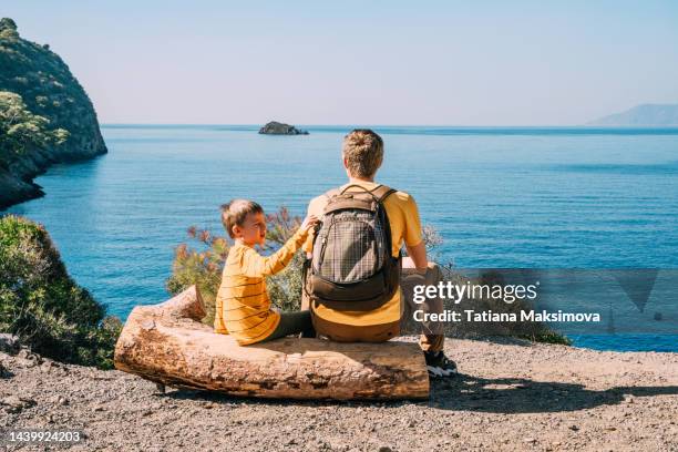 father and son in yellow t-shirts with backpack is enjoying the sea view. - fun sommer berge stock-fotos und bilder