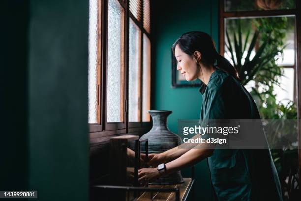 young asian woman decorating and arranging picture frames and home decorations over the cabinet at home. enjoying her time at cozy home - home design colors stockfoto's en -beelden