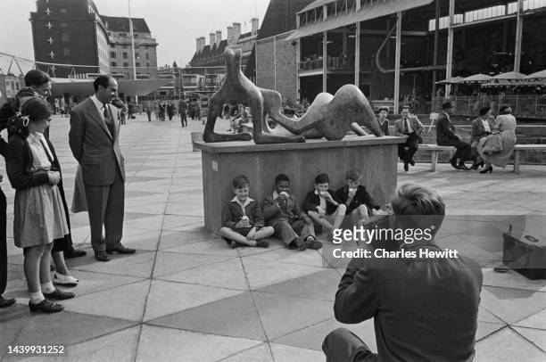 American pianist and singer Sugar Chile Robinson poses with three boys, all four lean up against the plinth on which is a reclining figure by Henry...
