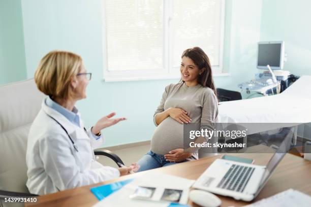 glückliche schwangere frau, die mit ihrem gynäkologen im büro spricht. - pregnant woman at doctor stock-fotos und bilder