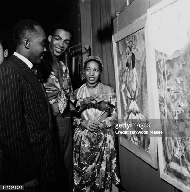 Man in a pinstripe suit with Trinidadia musician, dancer and artist Boscoe Holder and his wife, Trinidadia dancer Sheila Davis Clarke, both wearing...