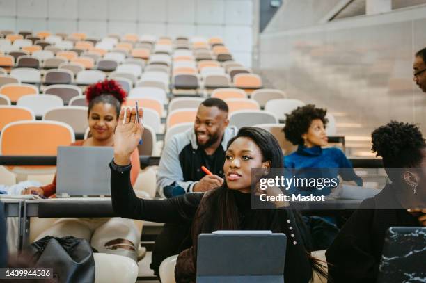 young female student raising hand during lecture in class - aula de conferencias fotografías e imágenes de stock