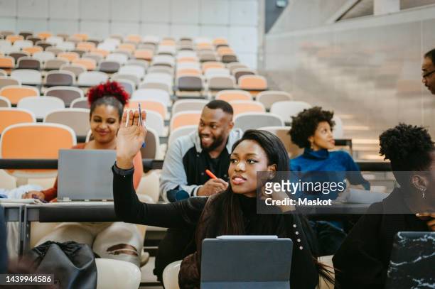 young female student raising hand during lecture in class - attending college stock pictures, royalty-free photos & images