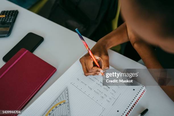 high angle view of student doing mathematics lesson on notebook at desk in classroom - spiral notebook stock pictures, royalty-free photos & images