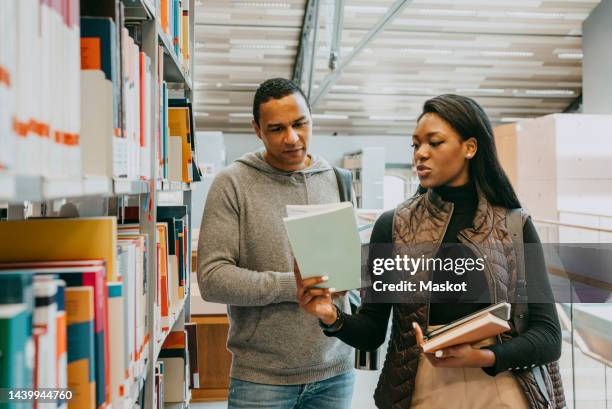 woman showing book to friend standing near shelf in library - choosing a book stock pictures, royalty-free photos & images