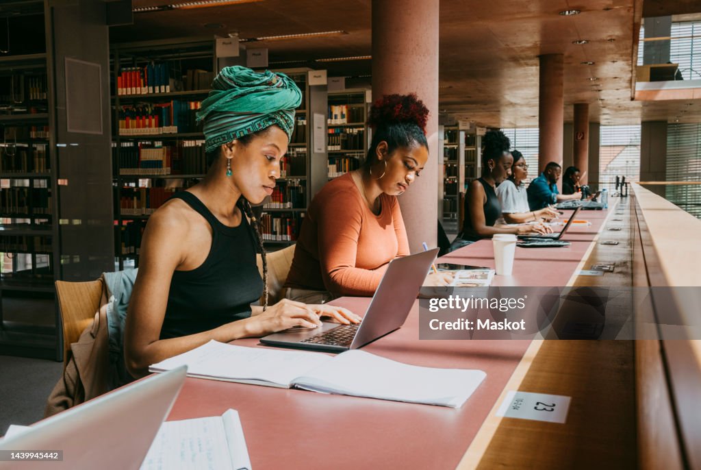 Woman wearing turban using laptop while sitting with friend in library