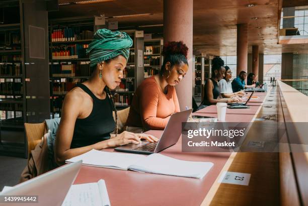 woman wearing turban using laptop while sitting with friend in library - post secondary education stock pictures, royalty-free photos & images
