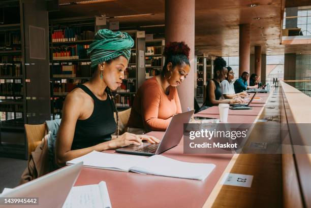 woman wearing turban using laptop while sitting with friend in library - tech stock pictures, royalty-free photos & images