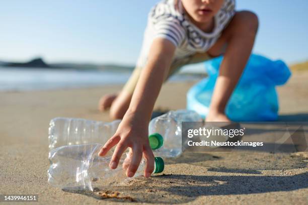 un enfant militant ramasse une bouteille d’eau abandonnée - sac en plastique photos et images de collection