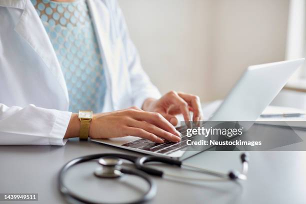 female doctor typing on laptop at desk in hospital - typing stock pictures, royalty-free photos & images