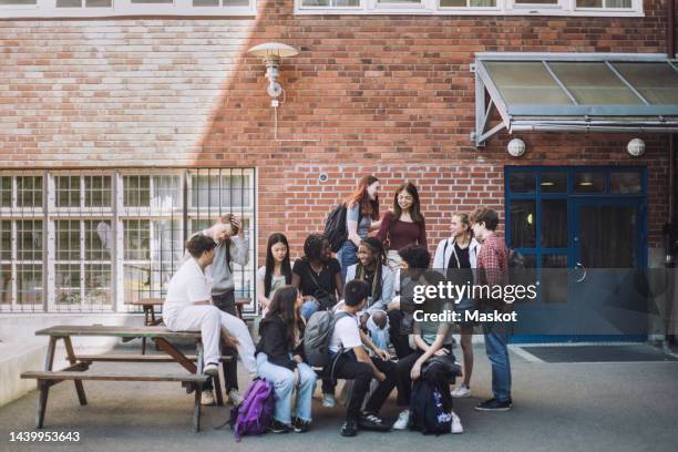 multiracial male and female friends sitting in campus during break time at junior high school - schoolplein stockfoto's en -beelden