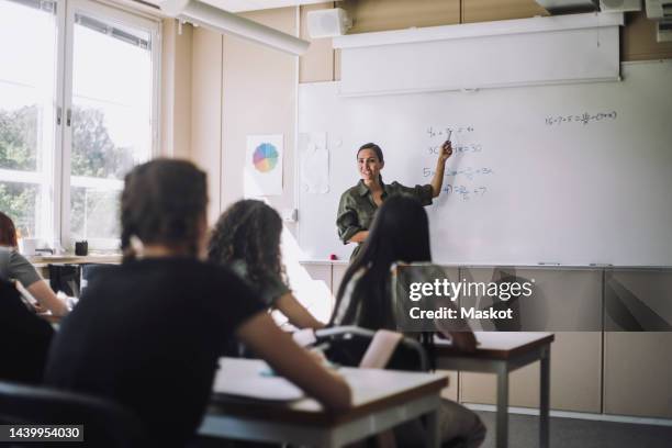 smiling teacher explaining mathematical formula to female students in classroom - maestra foto e immagini stock