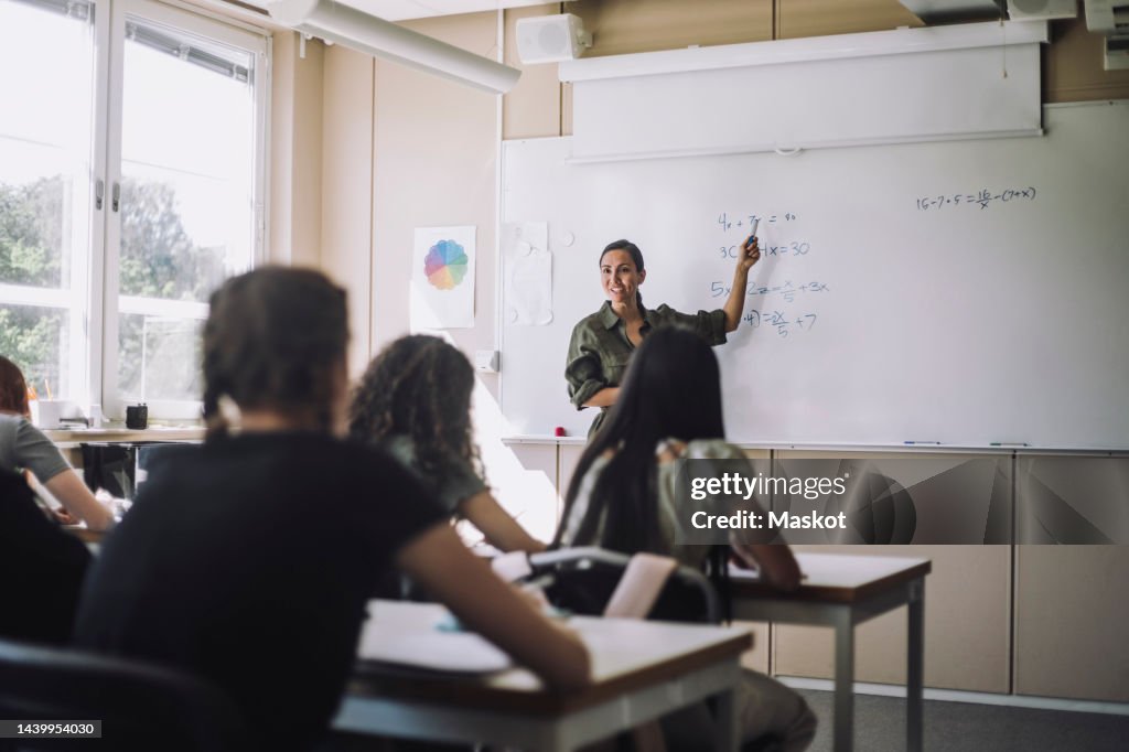 Smiling teacher explaining mathematical formula to female students in classroom