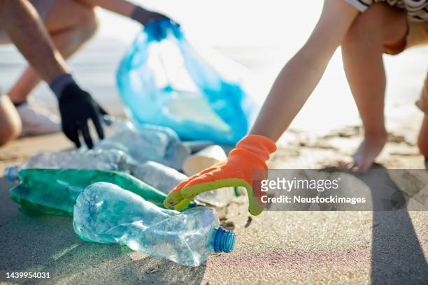 boy and father wearing gloves collecting bottles - plastic pollution beach stock pictures, royalty-free photos & images
