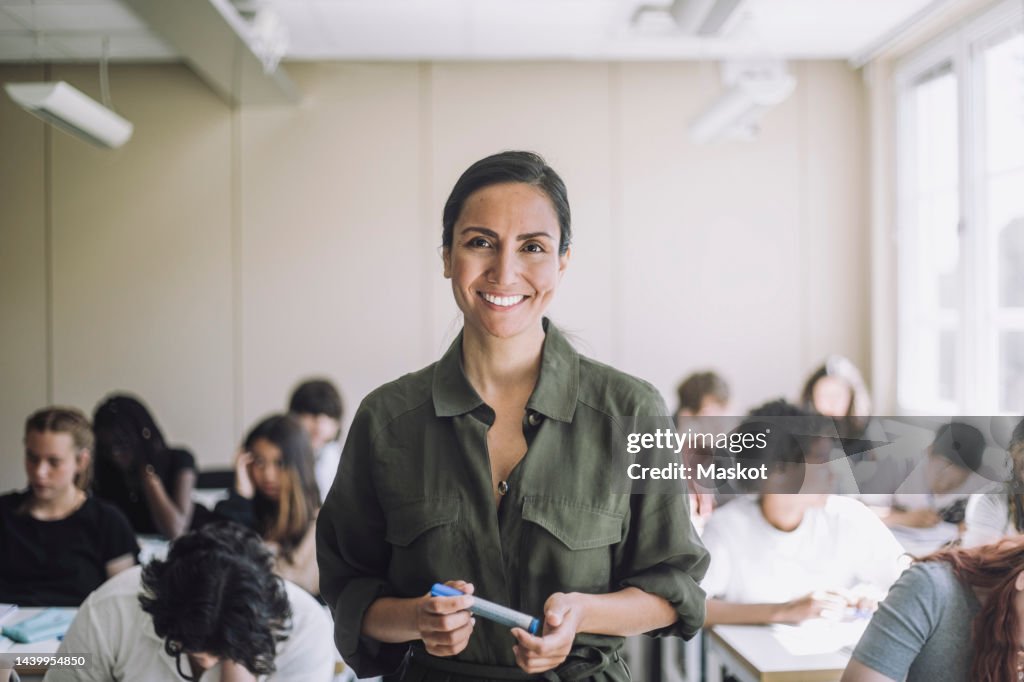 Portrait of happy female teacher with students in background at school