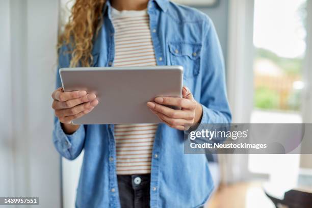 midsection of woman holding tablet pc at home - denim shirt stock pictures, royalty-free photos & images