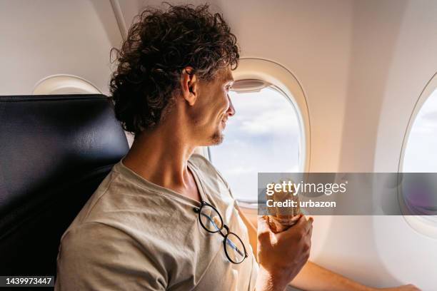 young man eating a sandwich in an airplane - plane food stock pictures, royalty-free photos & images