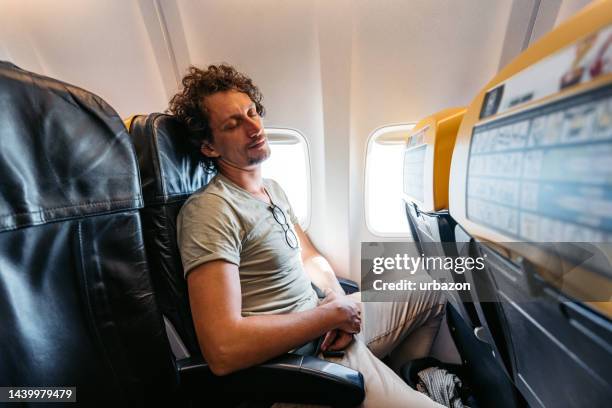 junger mann schläft in einem flugzeug - flugzeugsitz stock-fotos und bilder