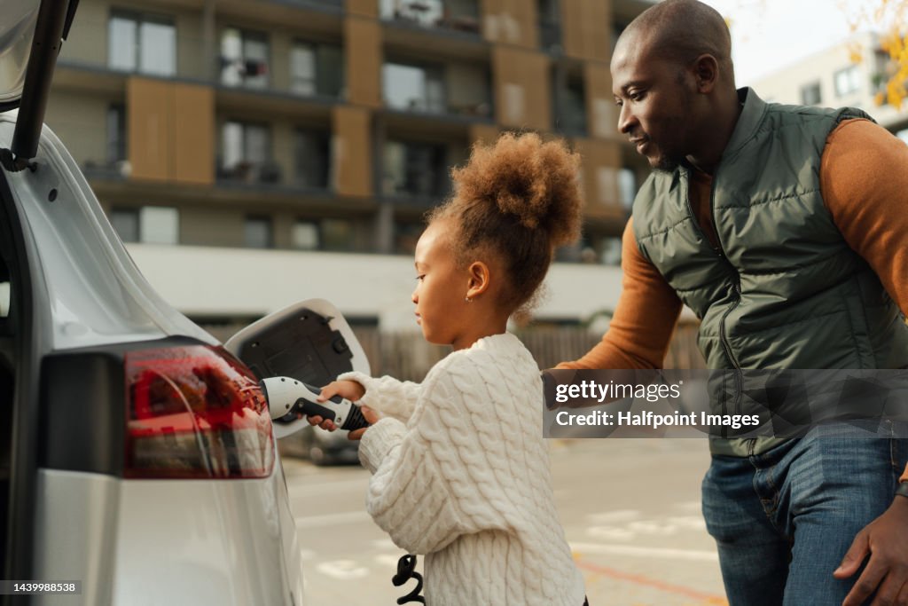 Close-up of father with his daughter charging their electric car.