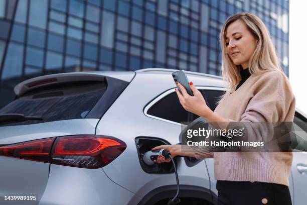 young woman waiting for car charging. - coche eléctrico coche de combustible alternativo fotografías e imágenes de stock