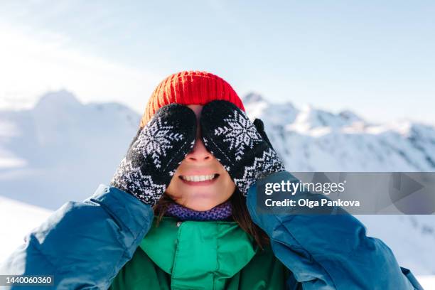 woman has fun and covers her eyes with her hands dressed in mittens in the mountains in winter - woman hands in mittens stock-fotos und bilder