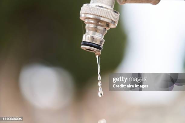 close-up of a drop falling from drinking water faucet, blurred background in open air - water wastage stock pictures, royalty-free photos & images