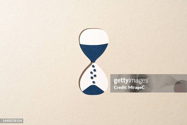blue hourglass passing time on beige paper cut craft - reloj de arena fotografías e imágenes de stock