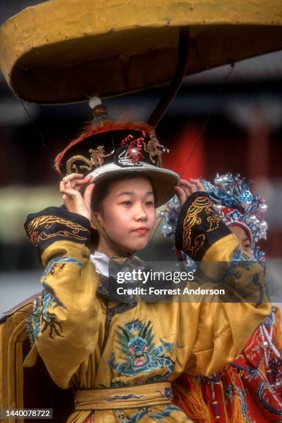 Close-up a girl as she adjusts the brim of a hat from a Qing dynasty costume as she poses for a photo in the Forbidden City, Beijing, China, 1990s.
