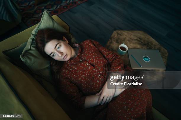 portrait of a long-haired red-haired woman lying down on the sofa with cup of tea - zyklus stock-fotos und bilder