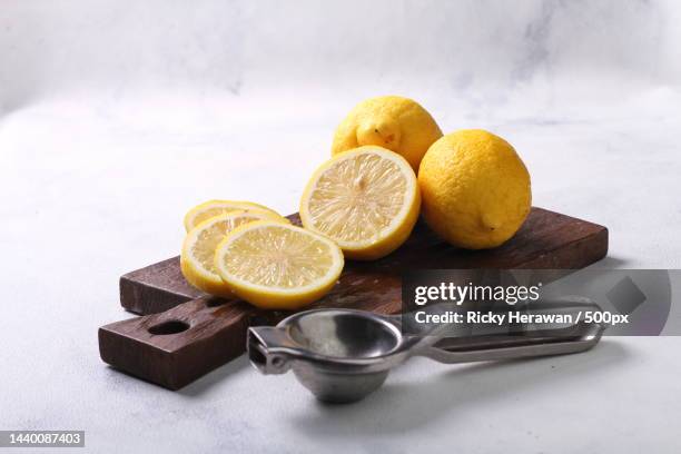 close-up of lemon slices and juice squeezer on wooden slab and white table - juice extractor stock pictures, royalty-free photos & images